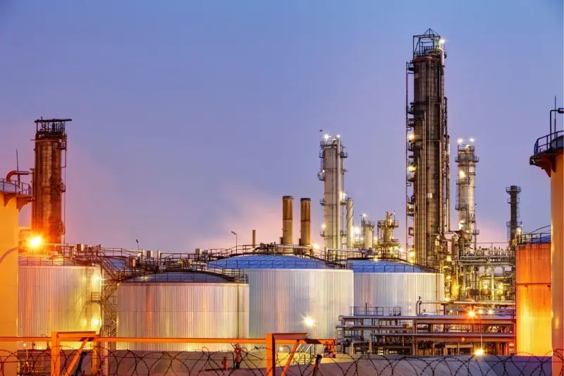 A group of large oil tanks in front of some towers.